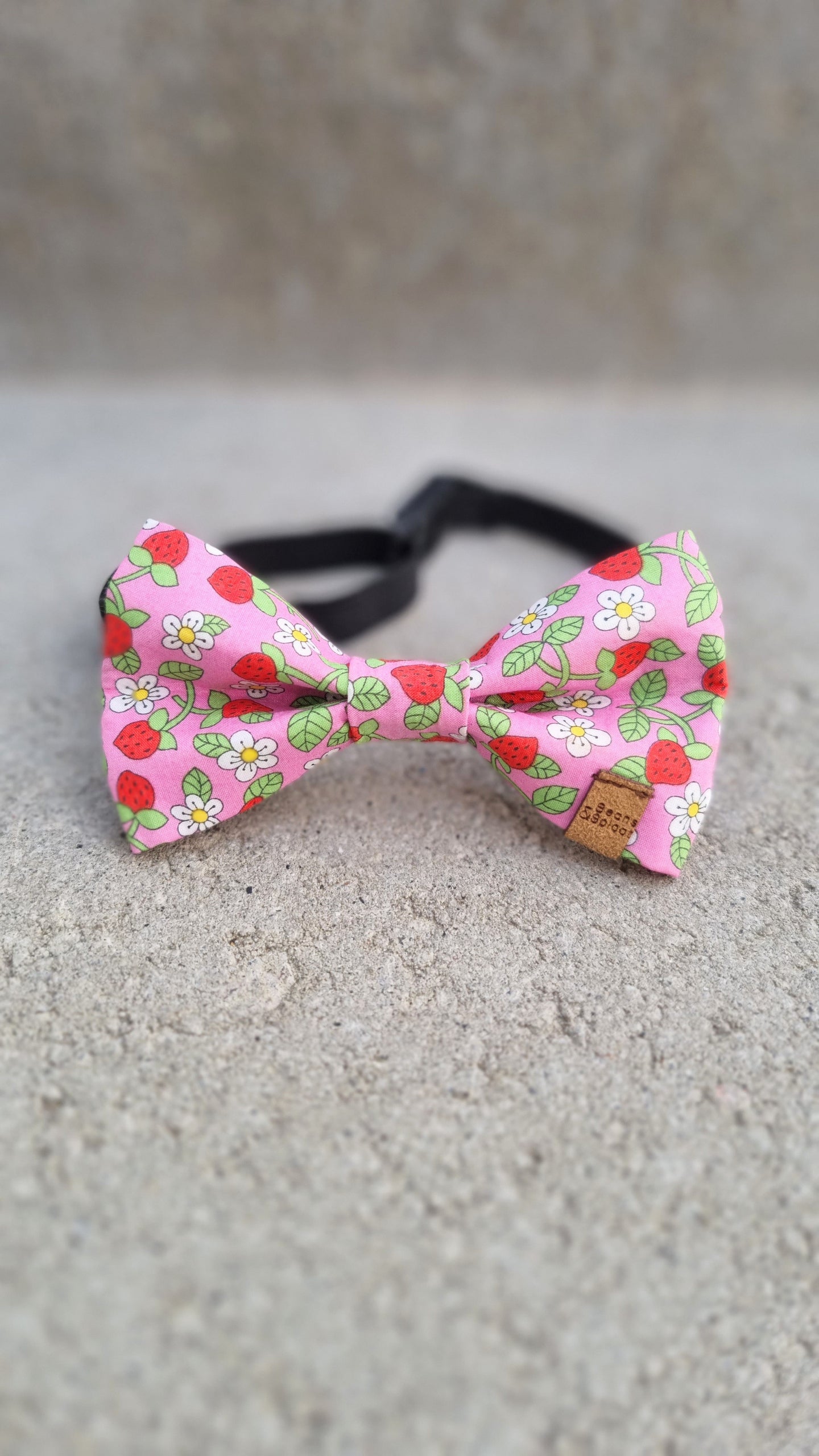 A pink dog bow tie with strawberry and white flower pattern.